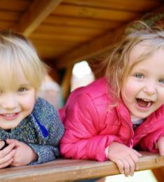 To børn sidder under et bordbænkesæt og smiler