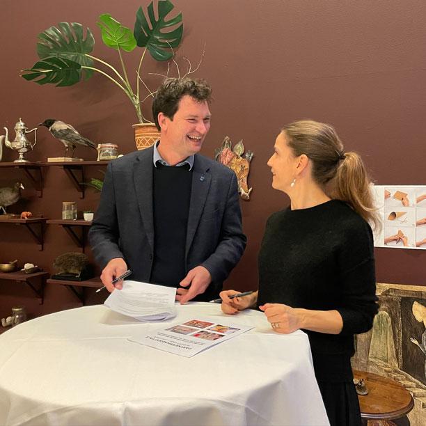 borgmester i Vallensbæk, Henrik Rasmussen, og direktør på ARKEN, Marie Nipper, står ved et rudnt cafébord og smiler til hinanden foran de underskrevne samarbejdsaftaler.
