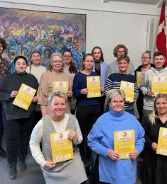 Gruppefoto af 13 kvinder og den mandlige underviser står og sidder med deres diplomer i hånden.