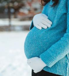 En gravid kvinde står i tyk trøje og holder med vanterne om sin mave. I baggrunden ligger der sne.