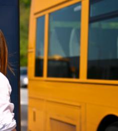 En kvinde står ved busstoppested, mens gul bus kører forbi hende.