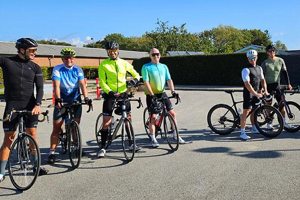 Seks mænd er hoppet af sadlen på deres cykler til landevejskørsel. De fleste bærer hjem, cykelshorts og cykelsko