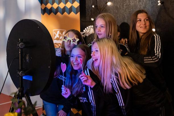 En gruppe unge, storsmilende piger står foran en selfieudløser og laver et gruppefoto.