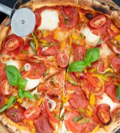 En pizza på et rundt spækbræt. Det er en pepperonipizza med tomat, basilikum og peberfrugt