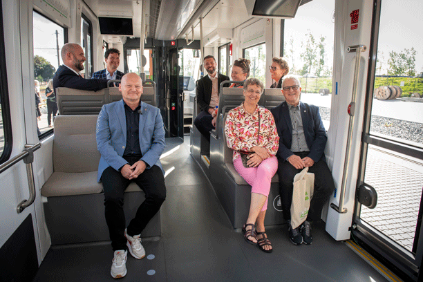 En gruppe borgmestre sidder i ny togvogn og smiler til hinanden og kameraet.