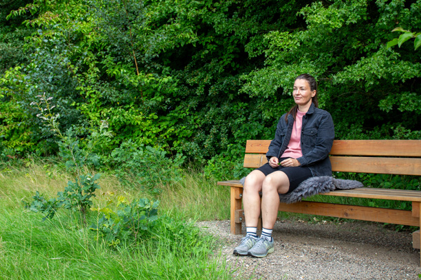 Kvinde sidder på bænk i et grønt område