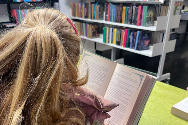 En pige læser i en tyk bog på et bibliotek